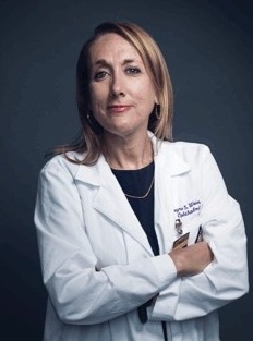 Professional headshot of a person wearing a white medical coat over a dark top, with arms crossed against a dark blue background. Provide your feedback on BizChat