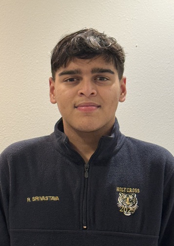 Head-and-shoulders portrait of a person with short, dark hair wearing a dark quarter-zip fleece pullover. The person is facing the camera against a plain light-colored wall. Embroidered text on the pullover reads “R. SRIVASTAVA,” and a “Holy Cross” emblem is visible on the opposite side. The image is framed from the chest up and lit with even indoor lighting.