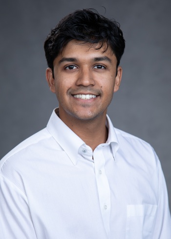 Professional headshot of a person wearing a white button-down shirt against a gray studio background.