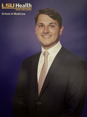Professional portrait of a person in a dark suit and striped tie against a blue background with LSU Health New Orleans School of Medicine branding.