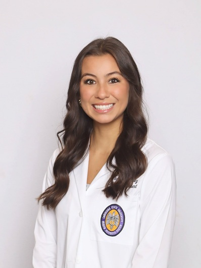 Professional medical school headshot showing a person wearing a white medical coat with embroidered text identifying the wearer as a medical student and a Louisiana State University Health Sciences Center emblem on the chest pocket. A small lapel pin is attached to the coat. The subject is facing the camera against a plain light gray background with even, professional lighting.