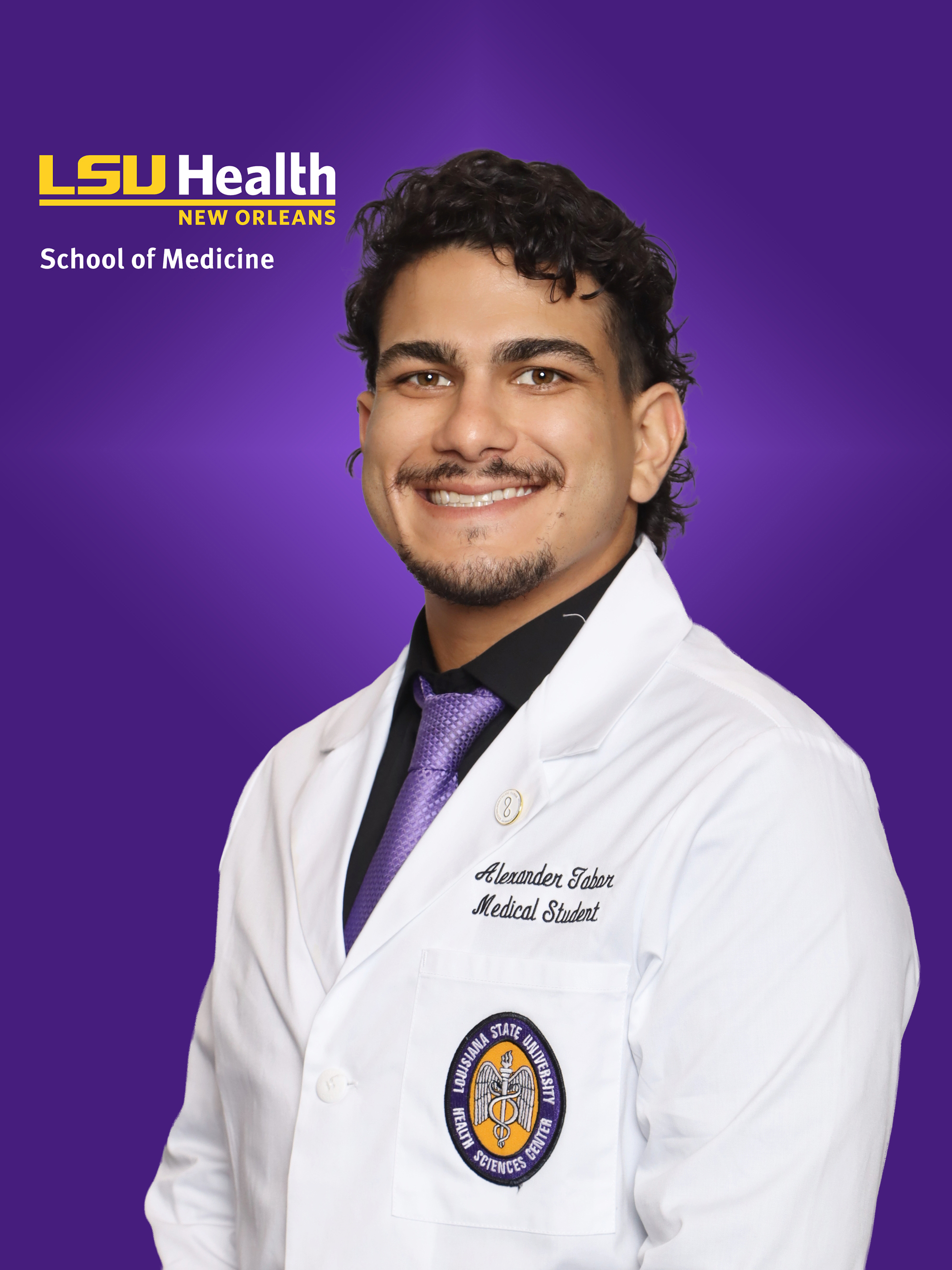 Professional medical school headshot showing a person wearing a white medical coat over a black dress shirt and a purple tie. Visible embroidered text on the coat includes the title “Medical Student,” and a Louisiana State University Health Sciences Center emblem is displayed on the chest pocket. A circular lapel pin is attached to the coat. The portrait is set against a purple LSU Health New Orleans School of Medicine branded background with the LSU Health New Orleans logo and “School of Medicine” text visible in the upper left corner.